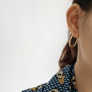 Close-up of elegant gold twisted hoop earring worn by a model in a minimalist style