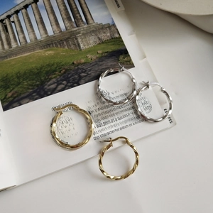 Detailed view of twisted knot hoop earrings in gold and silver on a fashion magazine