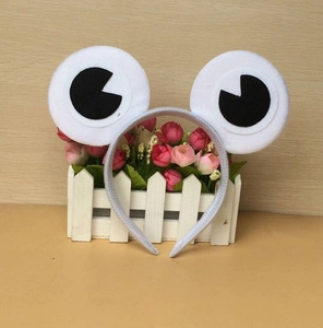 Detail of plush frog headband with big cartoon eyes displayed in a white garden fence prop
