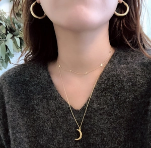 Close-up of model wearing gold layered moon necklace, star choker and hoop earrings