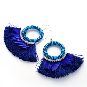 Primer plano de pendientes bohemios azules con plumas, cuentas y flecos detallados