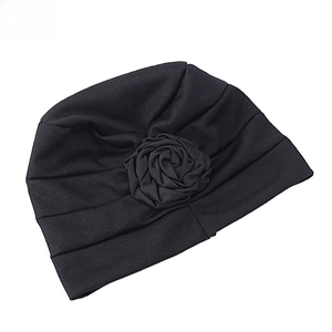 Gros plan d'un bonnet turban noir orné d'une grande fleur de rose en tissu plissé