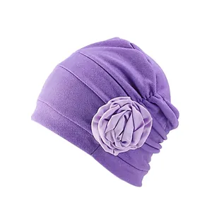 Vue détaillée d'un turban violet foncé plissé avec une grande fleur décorative latérale