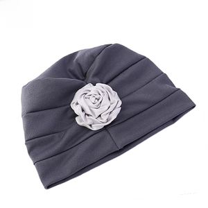 Détail du turban plissé gris foncé orné d'une fleur décorative en tissu gris clair