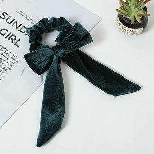 Detail of dark green velvet bow scrunchie with metallic sheen on a clean white desk
