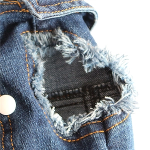 Detail of distressed dark blue denim dog vest featuring orange stitching and a white button