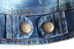 Detailed macro view of denim pet vest with yellow stitching and vintage metal buttons