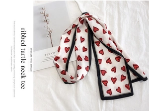 Close-up of long narrow silk scarf featuring red heart patterns and black contrast borders