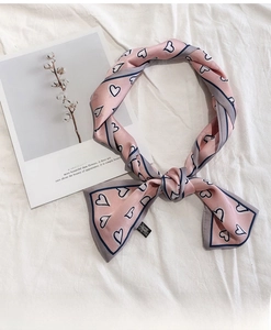 Detailed close-up of 100% silk pink skinny scarf with heart patterns and material label