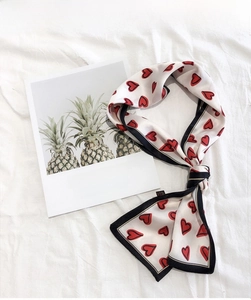 Detail of a white silk twilly scarf with red heart patterns and black contrast piping
