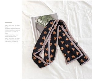 Detail of a narrow black silk scarf featuring heart patterns on white fabric