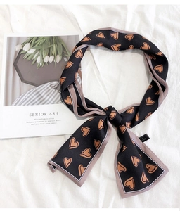 Detail of silk twilly scarf with heart print tied in a bow on a soft white texture