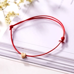 Macro detail of a red woven rope bracelet with a polished gold heart charm