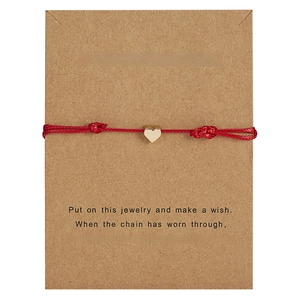 Detail of red braided wish bracelet with gold heart charm on brown display card