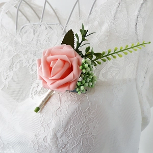 Boutonnière rose en mousse PE avec baies vertes sur une robe de mariée en dentelle blanche
