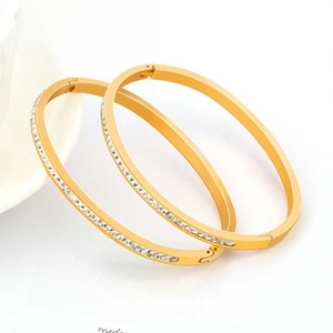 Close-up of golden flat bangles with rows of white crystals on a minimal background
