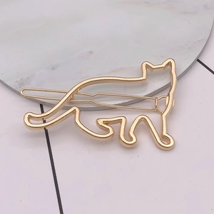 Detail view of a golden cat-shaped metal hair clip on a marble pedestal with pink background