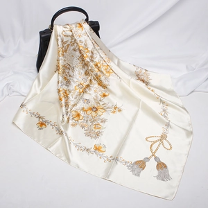Elegant beige silk-like scarf with gold floral patterns draped over a black leather handbag
