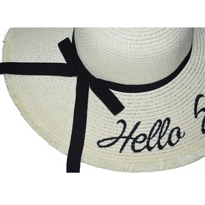 Detail of cream straw sun hat featuring black 'Hello' embroidery and fringed brim