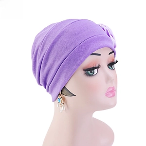 Détail du turban violet montrant le tissu plissé doux et l'ornement fleur en satin