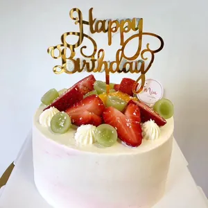 Close-up of golden acrylic Happy Birthday cake topper on a fresh fruit and cream cake