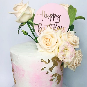 Close-up of a birthday cake with white roses, gold foil, and pink acrylic Happy Birthday topper