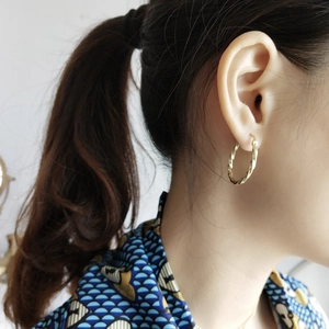 Close-up of a model wearing minimalist golden twisted rope hoop earrings in 925 silver