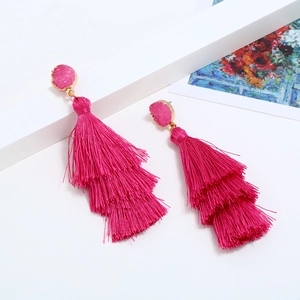 Close-up of pink tiered tassel earrings with gold framed stone on a white surface