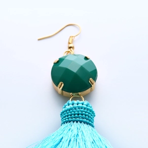 Detalle de pendientes bohemios con piedras verdes y borlas de color azul claro