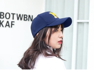 Detail view of the yellow embroidered letter M on the side of a navy blue cotton baseball cap