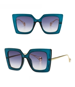 Detail of blue square sunglasses featuring gradient lenses and gold temples with pearls