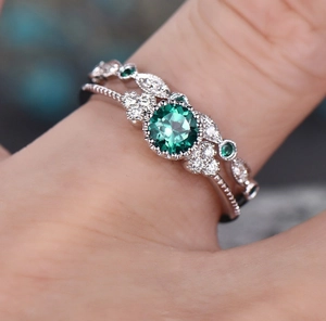 Detail of emerald green gemstone ring set with micro-pawn diamonds on female hand