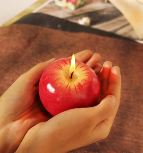 Primer plano de una vela realista con forma de manzana roja encendida con llama cálida