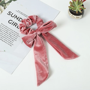 Elegant dried rose velvet scrunchie with long bow ribbon on a minimalist white table