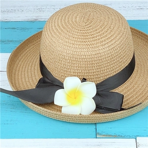 Straw beach hat with wide black ribbon and white frangipani flower on blue wooden board