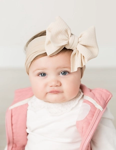 Close-up of a baby wearing a soft beige nylon headband with a waffle texture bow