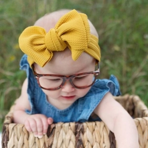 Detailed view of a baby girl wearing a bright yellow textured fabric bow headband