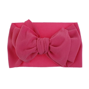 Detailed macro view of the bright pink ribbed fabric and oversized bow on a baby headband.