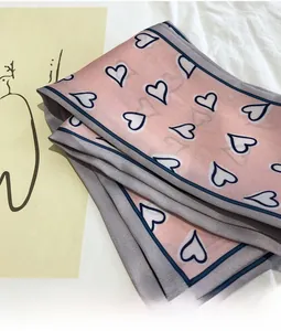 Close-up of pink silk scarf featuring navy blue heart patterns and border finish