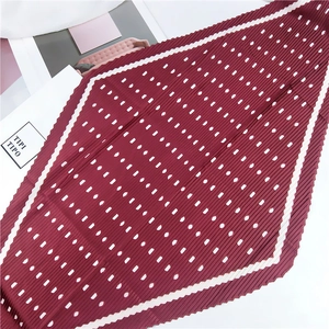 Détail d'un foulard en soie plissé bordeaux avec pois blancs et bordure élégante