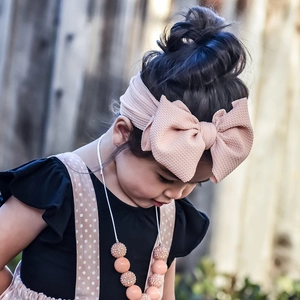 Detailed view of a baby girl wearing a large pink textured fabric bow headband