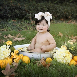 Close-up detail of a cute smiling baby wearing a large cream fabric bow headband outdoors