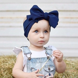 Close-up view of a baby girl wearing a large navy blue bow headband in a straw field.