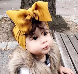 Close-up of a mustard yellow textured bow headband worn by a cute baby girl.