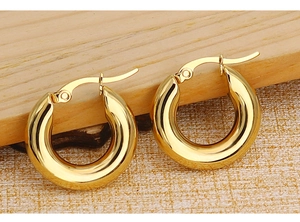 Macro shot of polished gold chunky hoop earrings with a latch-back closure on wood texture