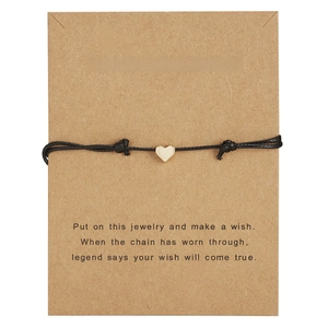 Minimalist black braided cord bracelet with polished gold heart pendant on kraft card