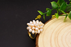 Vue détaillée d'une bague fleur dorée avec perles baroques blanches naturelles sur bois