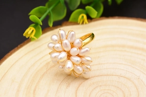 Détail d'une bague de perles blanches tissées de fils dorés sur un support en bois naturel
