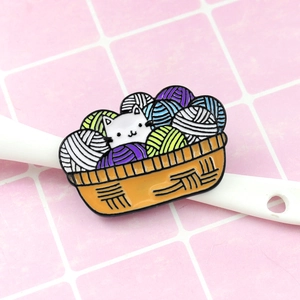 Cute white cat enamel pin popping out from an orange basket filled with colorful yarn balls