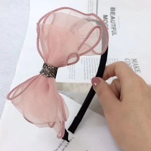 Close-up of pink lace bow headband with black rhinestones held against a magazine